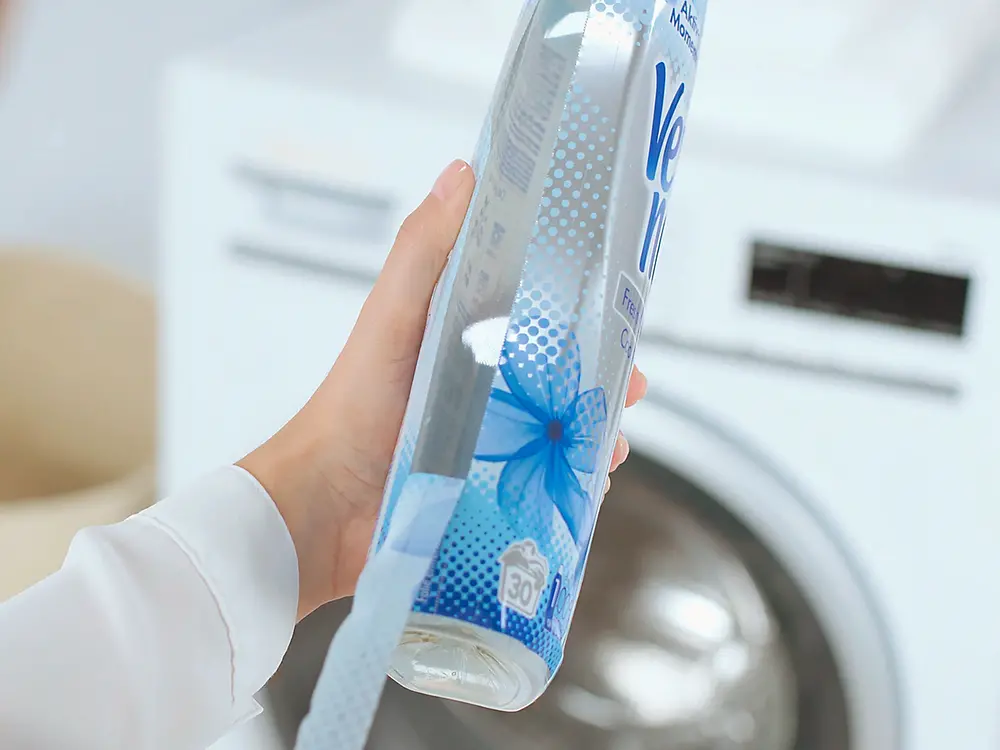 A person seen from behind removes a thin film jacket from a Vernel bottle.